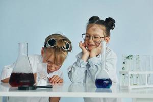 Mädchen mit Jungen, die zusammenarbeiten. Kinder in weißen Mänteln spielen einen Wissenschaftler im Labor, indem sie Geräte verwenden foto