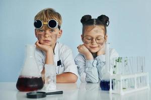 Mädchen mit Jungen, die zusammenarbeiten. Kinder in weißen Mänteln spielen einen Wissenschaftler im Labor, indem sie Geräte verwenden foto