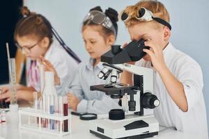 Mikroskop verwenden. Kinder in weißen Mänteln spielen einen Wissenschaftler im Labor, indem sie Geräte verwenden foto