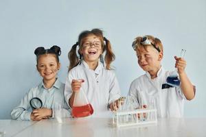 glückliche Freunde lächeln. Kinder in weißen Mänteln spielen einen Wissenschaftler im Labor, indem sie Geräte verwenden foto