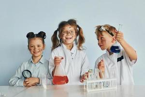 glückliche Freunde lächeln. Kinder in weißen Mänteln spielen einen Wissenschaftler im Labor, indem sie Geräte verwenden foto