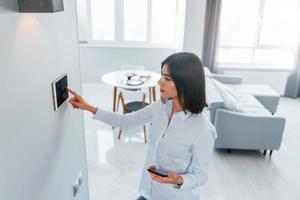 verwendet Tablet, das in der Wand montiert wird. junge frau ist tagsüber drinnen im smart house room foto