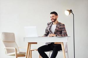 sitzt am Tisch im Büro. junger stilvoller geschäftsmann im anzug drinnen. Vorstellung von Erfolg foto