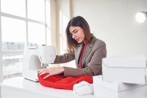 Näherin arbeitet mit rotem Tuch. junge Frau in formeller Kleidung ist drinnen. Vorstellung von Stil foto