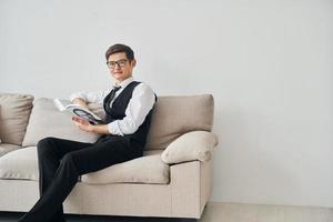 junger mann in formeller kleidung sitzt drinnen auf dem sofa gegen die weiße wand foto