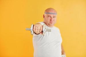 Übungen mit Hanteln. lustiger übergewichtiger mann in sportlicher kopfbindung ist vor gelbem hintergrund foto