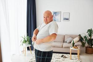 Taille messen. lustiger übergewichtiger mann in lässiger kleidung ist drinnen zu hause foto