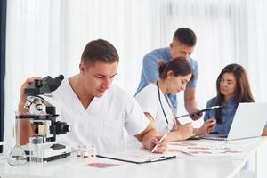 Mann mit Mikroskop. Gruppe junger Ärzte arbeitet in der modernen Praxis zusammen foto