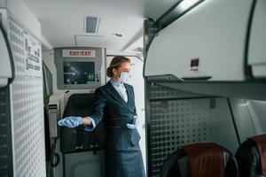 in Schutzhandschuhe und Maske. junge Stewardess über die Arbeit im Passagierflugzeug foto