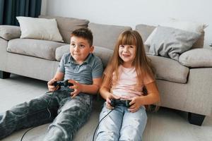 Videospiele spielen. Kinder, die sich tagsüber gemeinsam im Wohnzimmer amüsieren foto