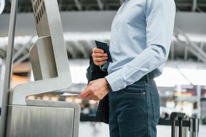 Terminal verwenden. Der junge Geschäftsmann in formeller Kleidung ist tagsüber am Flughafen foto