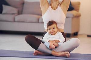 auf der Yogamatte. Mutter mit ihrer kleinen Tochter ist zusammen zu Hause foto