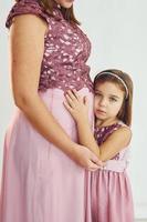 Frau ist schwanger. Mutter im Kleid steht mit ihrer Tochter im Studio mit weißem Hintergrund foto