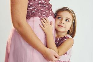 Frau ist schwanger. Mutter im Kleid steht mit ihrer Tochter im Studio mit weißem Hintergrund foto