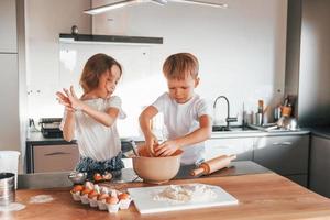 mit Teig arbeiten. kleiner Junge und Mädchen, die Weihnachtsplätzchen in der Küche zubereiten foto