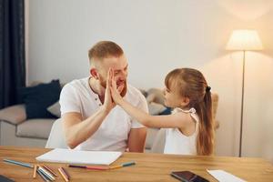 am Tisch sitzen und Spaß haben. Vater mit seiner kleinen Tochter ist zusammen zu Hause foto