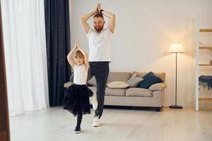 Yoga-Posen. Vater mit seiner kleinen Tochter ist zusammen zu Hause foto