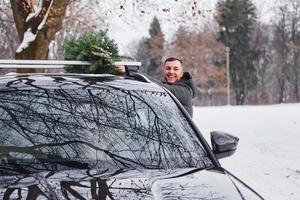 Vorbereitung auf das Wochenende. mann mit kleiner grüner tanne ist draußen in der nähe seines autos. Konzeption von Feiertagen foto