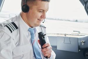 spricht mit einem Mikrofon. Pilot in formeller Kleidung sitzt im Cockpit und steuert Flugzeug foto