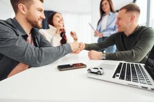 Handschlag machen. Gruppe von Menschen arbeitet im Büro, indem sie am Tisch sitzen foto