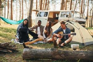 Lager und Auto. Gruppe junger Leute ist tagsüber gemeinsam im Wald unterwegs foto