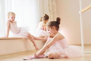 Mädchen sitzt auf dem Boden. kleine Ballerinas bereiten sich auf den Auftritt vor, indem sie Tanzbewegungen üben foto