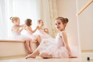 Mädchen sitzt auf dem Boden. kleine Ballerinas bereiten sich auf den Auftritt vor, indem sie Tanzbewegungen üben foto