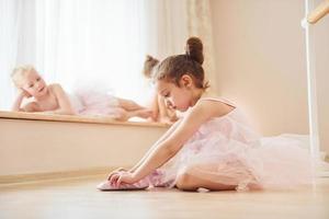 Mädchen sitzt auf dem Boden. kleine Ballerinas bereiten sich auf den Auftritt vor, indem sie Tanzbewegungen üben foto