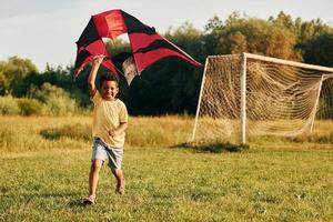 spielen mit drachen. afroamerikanisches kind hat tagsüber im sommer spaß auf dem feld foto