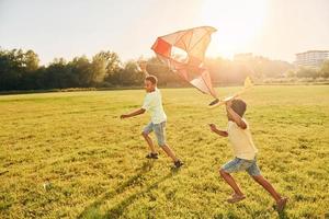 Laufen mit Drachen. Zwei afroamerikanische Kinder haben im Sommer tagsüber gemeinsam Spaß auf dem Feld foto