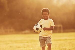 junger Fußballspieler. afroamerikanisches kind hat tagsüber im sommer spaß auf dem feld foto