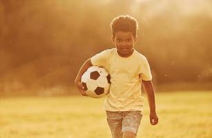junger Fußballspieler. afroamerikanisches kind hat tagsüber im sommer spaß auf dem feld foto