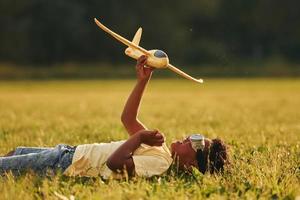 mit Spielzeugflugzeug auf dem Rasen niederlegen. afroamerikanisches kind hat tagsüber im sommer spaß auf dem feld foto