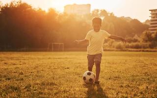 Spielt Fußball. afroamerikanisches kind hat tagsüber im sommer spaß auf dem feld foto
