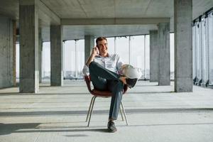 Konversation mit Telefon. junger mann in formeller kleidung arbeitet drinnen am bau foto