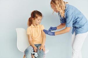 kleines Mädchen im gelben Hemd. Arzt in Uniform, der dem Patienten eine Impfung vornimmt foto