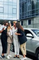 Frauen in formeller Kleidung stehen draußen in der Stadt zusammen in der Nähe eines silberfarbenen Autos foto