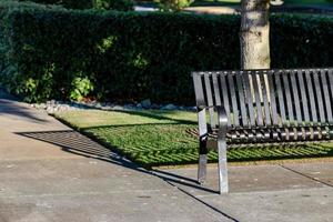 Parkbank wirft einen Schatten auf einen Gehweg foto