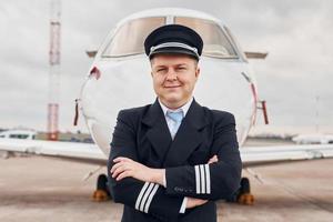 erfahrener pilot in uniform, der draußen in der nähe des flugzeugs steht foto