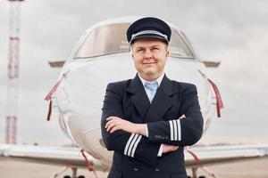 erfahrener pilot in uniform, der draußen in der nähe des flugzeugs steht foto