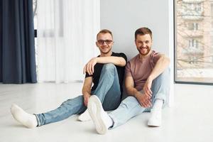 Zwei Freunde sitzen drinnen im modernen Wohnraum zusammen auf dem Boden foto