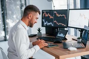 Konzentration auf die Arbeit. Der junge Geschäftsmann in formeller Kleidung ist mit mehreren Bildschirmen im Büro foto