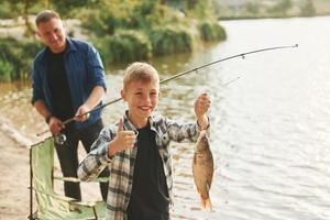 zeigt den Fang. Vater und Sohn beim gemeinsamen Angeln im Freien im Sommer foto