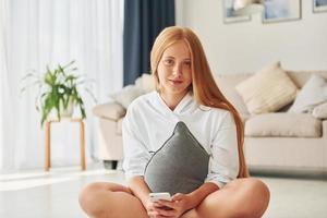 auf dem Boden sitzen. Teenagerin mit blonden Haaren ist tagsüber zu Hause foto