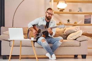 gemütliche Atmosphäre. Mann in Freizeitkleidung und mit Akustikgitarre ist drinnen foto