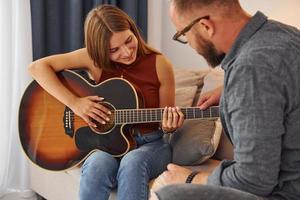 Privatunterricht. gitarrenlehrer, der jungen frau zeigt, wie man das instrument spielt foto