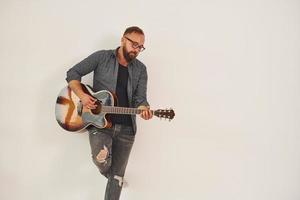 im Studio stehen. Mann in Freizeitkleidung und mit Akustikgitarre ist drinnen foto