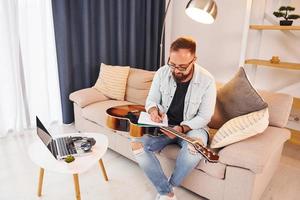 ein Lied machen. Mann in Freizeitkleidung und mit Akustikgitarre ist drinnen foto