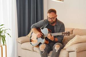 Mann in Freizeitkleidung und mit Akustikgitarre ist drinnen foto