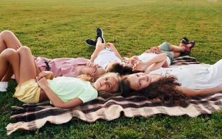 sich ausruhen und hinlegen. eine gruppe glücklicher kinder ist tagsüber draußen auf dem sportplatz foto